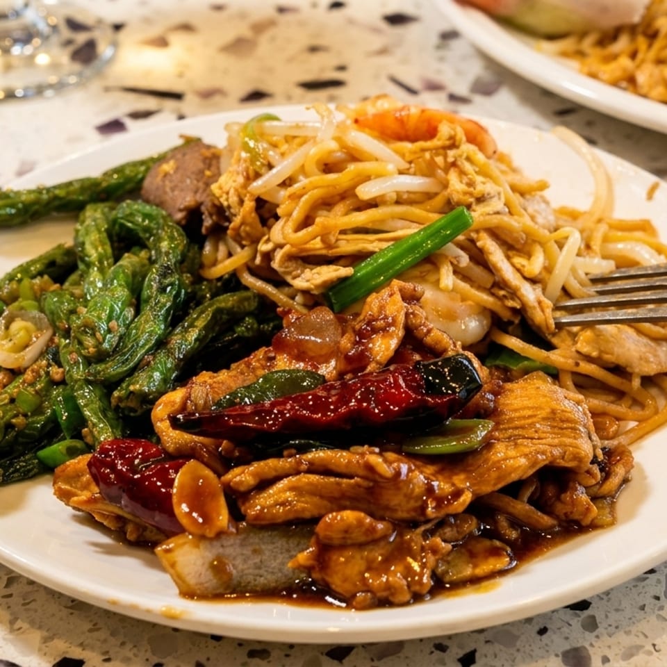Plate of stir-fried noodles, vegetables, meat, and dried chilies with a fork on a terrazzo restaurant table.