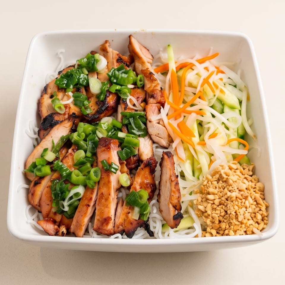 Vietnamese vermicelli bowl topped with grilled chicken, scallions, pickled vegetables, cucumber, carrots, and crushed peanuts.
