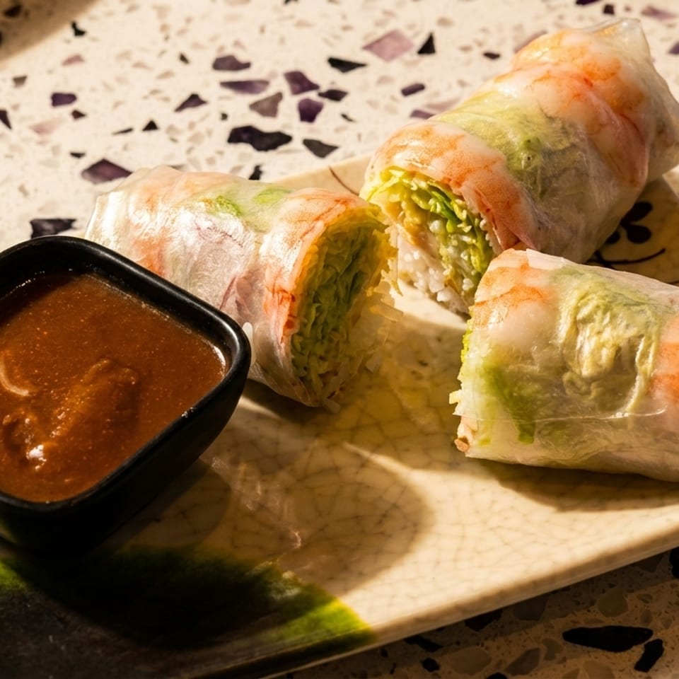 Three fresh Vietnamese spring rolls with shrimp, lettuce, and rice noodles served with dipping sauce on a rectangular plate.