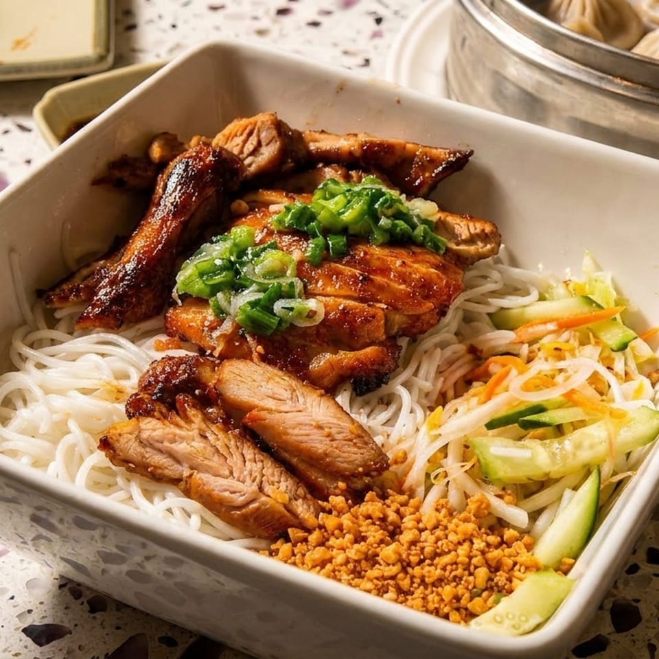 Vietnamese vermicelli bowl topped with grilled meats, scallions, vegetables, crushed peanuts, and fried shallots, beside steamed dumplings.